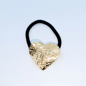 Detail of golden heart alloy hair tie with textured cross-hatch surface and black elastic band