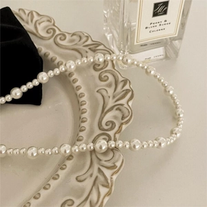 Elegant pearl necklace with varying sizes displayed on a vintage ceramic relief plate