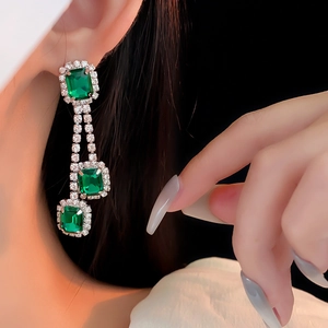 Close-up of emerald square gemstones dangling on vintage silver earrings with crystals