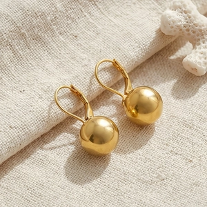 Detailed view of golden ball leverback earrings on a textured fabric and coral background