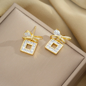 Golden bowknot cubic zirconia earrings displayed elegantly on a beige jewelry box lid