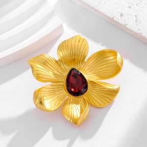 Detailed view of a gold flower brooch with a deep red teardrop crystal on white stones