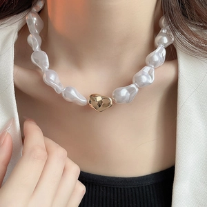 Détail d'un collier de perles baroques blanches avec une perle dorée au centre