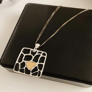 Détail d'un pendentif géométrique mat avec chaîne double épaisseur sur une boîte noire