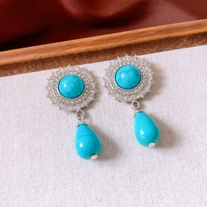 Detailed close-up of turquoise drop earrings with rhinestones on a white fabric surface