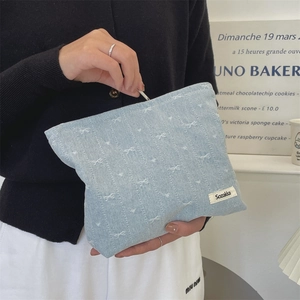 Detail of light blue denim makeup bag with white bow embroidery and zipper closure