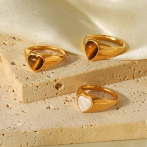 Close-up of 18k gold heart rings with tiger eye stone and white shell on satin