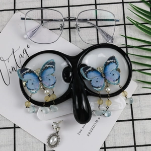Blue butterfly earring detail with pearls on black glass stand and plaid background