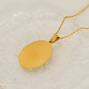 Macro shot of gold oval pendant with brushed metal texture on a textured glass surface