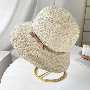 Elegant beige straw sun hat with pink ribbon bow displayed on a modern gold metal stand
