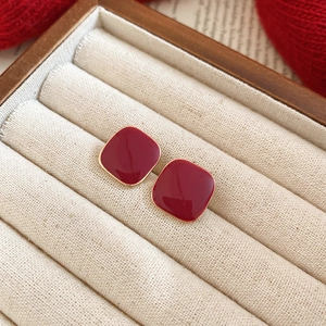 Elegant red square enamel stud earrings displayed in a beige jewelry box with red fabric