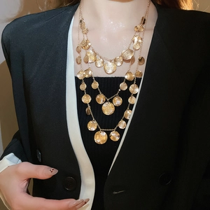 Close-up of a three-layer gold circular pendant necklace on a model with a black blazer