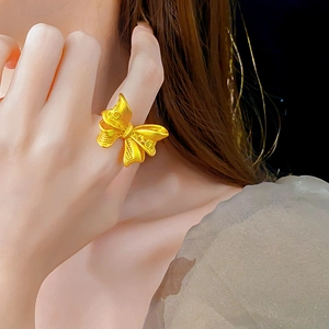 Detailed close-up of a gold bow ring with intricate brushed texture on a woman finger