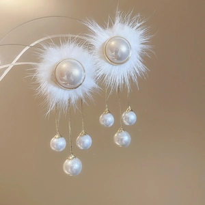 Close-up of pearl tassel earrings with white pom-poms and gold metal details
