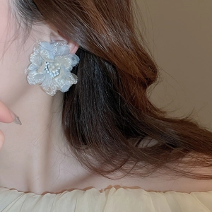 Close-up of model wearing light blue mesh flower earrings with central bead detail