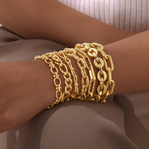 Detailed view of stacked 18K gold plated Figaro and Cuban link bracelets on a model's wrist