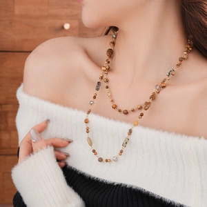 Close-up of layered glass bead necklace with earthy tones and gold chains on model