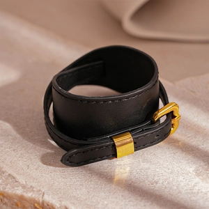 Detailed view of the black leather belt-style bracelet with polished gold buckle and stitching