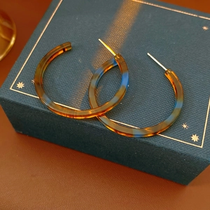 Macro di orecchini a cerchio in resina tartarugata su scatola regalo blu e fondo in pelle