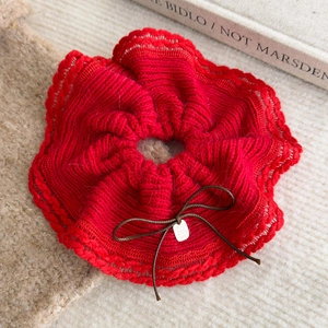 Close-up of a red knitted scrunchie with wave lace edge, bow, and a small metal tag