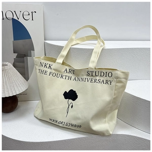 Close-up of canvas tote bag with black floral art and minimalist text on white studio stage