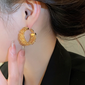 Close-up of gold hoop earring featuring a textured woven bird nest design on model