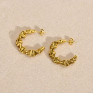 Detailed close-up of golden C-shaped twisted earrings with intricate wire-wrapped texture