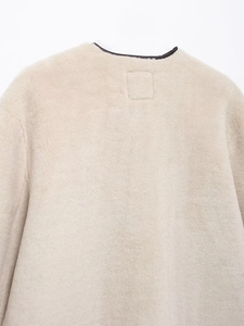 Dettaglio ravvicinato del cappotto beige in pelliccia sintetica con bordo scuro a contrasto