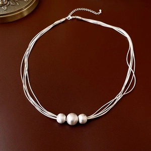 Layered silver necklace with three brushed beads on a dark leather surface