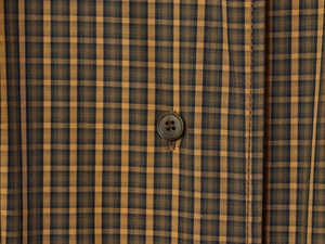 Detail of yellow and brown plaid fabric texture with dark brown button on shirt