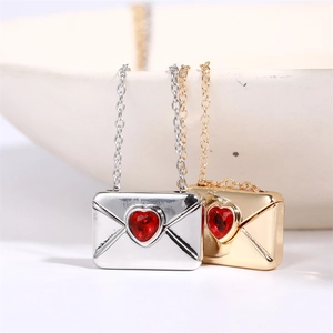 Detail of silver and gold envelope pendants with a red heart-shaped gemstone
