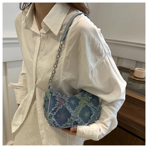Detailed view of blue denim underarm bag with star pattern and chain strap on shoulder
