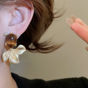 Macro view of matte gold fish tail stud earrings with brown resin stone and texture