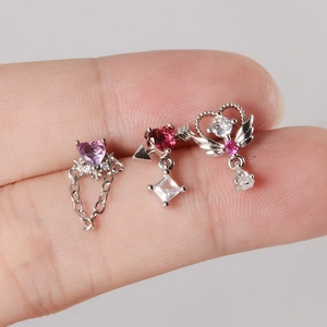 Macro detail of silver nose studs with pink and red heart-shaped zircon pendants on fingers