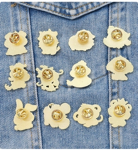 Macro detail of twelve zodiac enamel pins with gold butterfly clutch backs on denim
