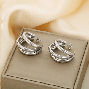 Detail view of silver triple-layered hoop earrings on a beige box and silk background