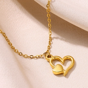 Gros plan détaillé d'un collier doré à double cœur sur un fond de soie champagne