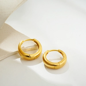 Detailed close-up of chunky 18K gold hoop earrings on minimalist stone background
