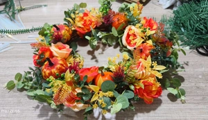 Detail of autumn wreath with orange roses, pumpkins, and foliage on a wooden surface
