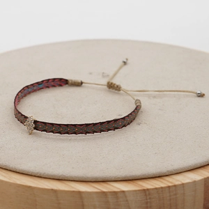Detail of hand-woven geometric bracelet with diamond-set gold charm and pull-string closure