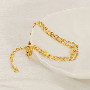 Gold double-layered stainless steel chain bracelet with small heart pendant on ceramic dish
