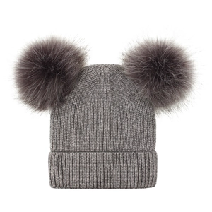 Detail of grey ribbed knit beanie featuring two fluffy faux fur pom-poms on white background