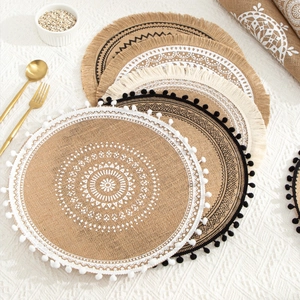 Detail of round jute placemats with ethnic patterns and tassels on a beige table