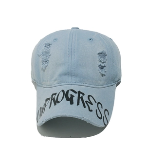 Detail of light blue distressed denim baseball cap with PROGRESS printed on the brim