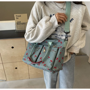 Side view of gray-blue nylon tote bag with red cherry print and wide shoulder strap