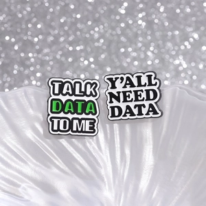 Detailed shot of two enamel pins with 'TALK DATA TO ME' and 'Y'ALL NEED DATA' phrases