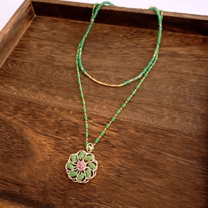 Macro shot of 18k gold plated floral pendant with green marquise stones and beaded chain