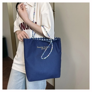 Detalle del bolso tote de lona azul con correa de cuentas y forro de cuadros azules