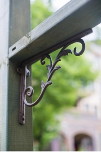 Close-up of vintage cast iron bracket with ornate scroll leaf texture on wood beam