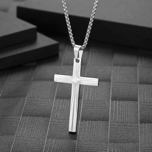 Minimalist silver cross necklace with sunburst texture hanging on black geometric stairs